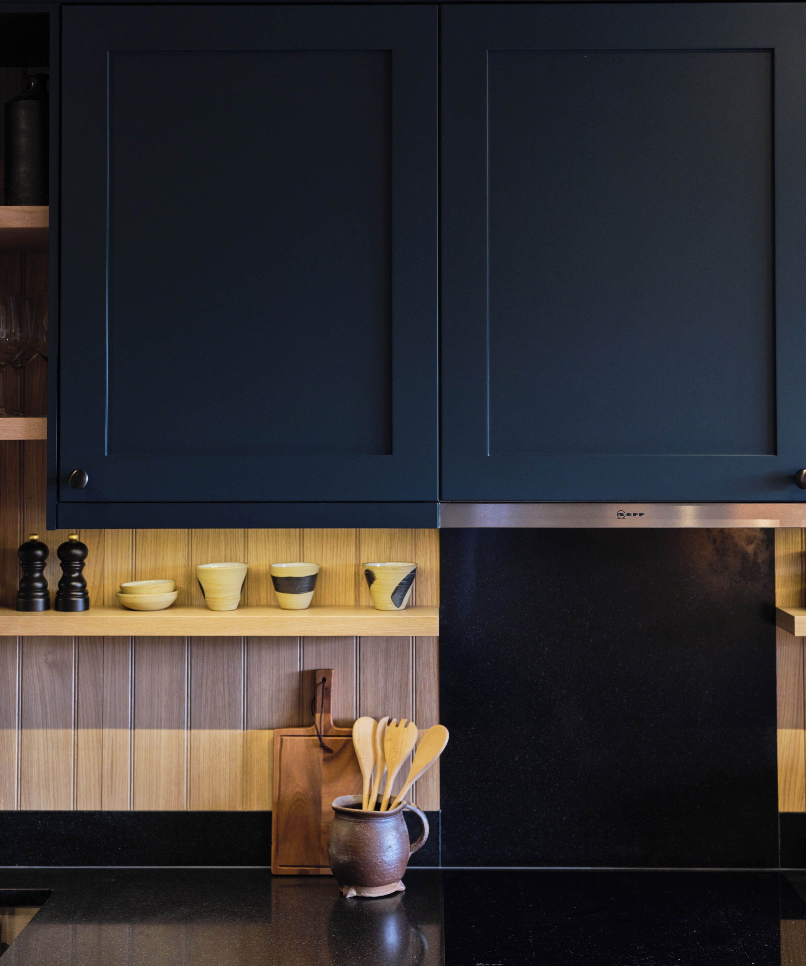 Una cocina con armarios oscuros, estantes de madera y una encimera negra.
