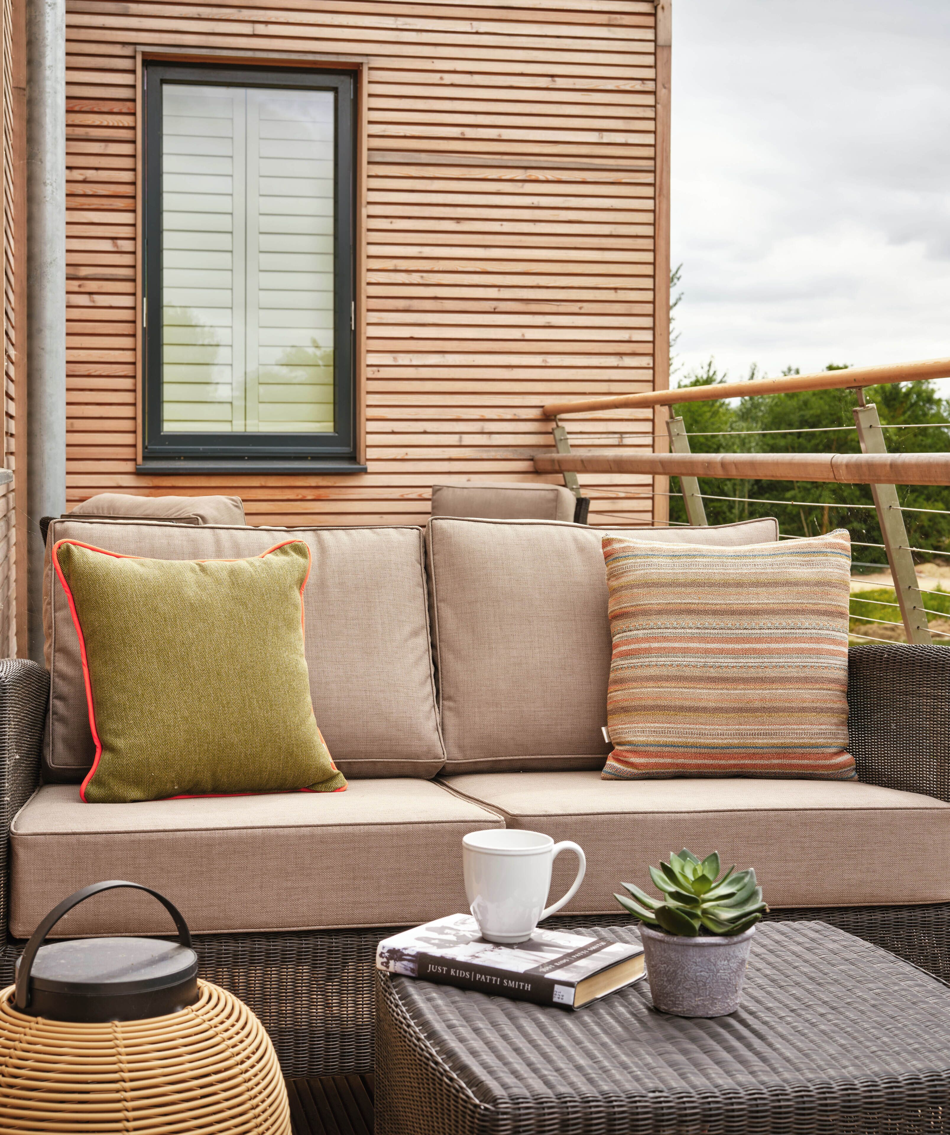A cozy outdoor seating area with a cushioned bench, a wicker table, and a potted plant.