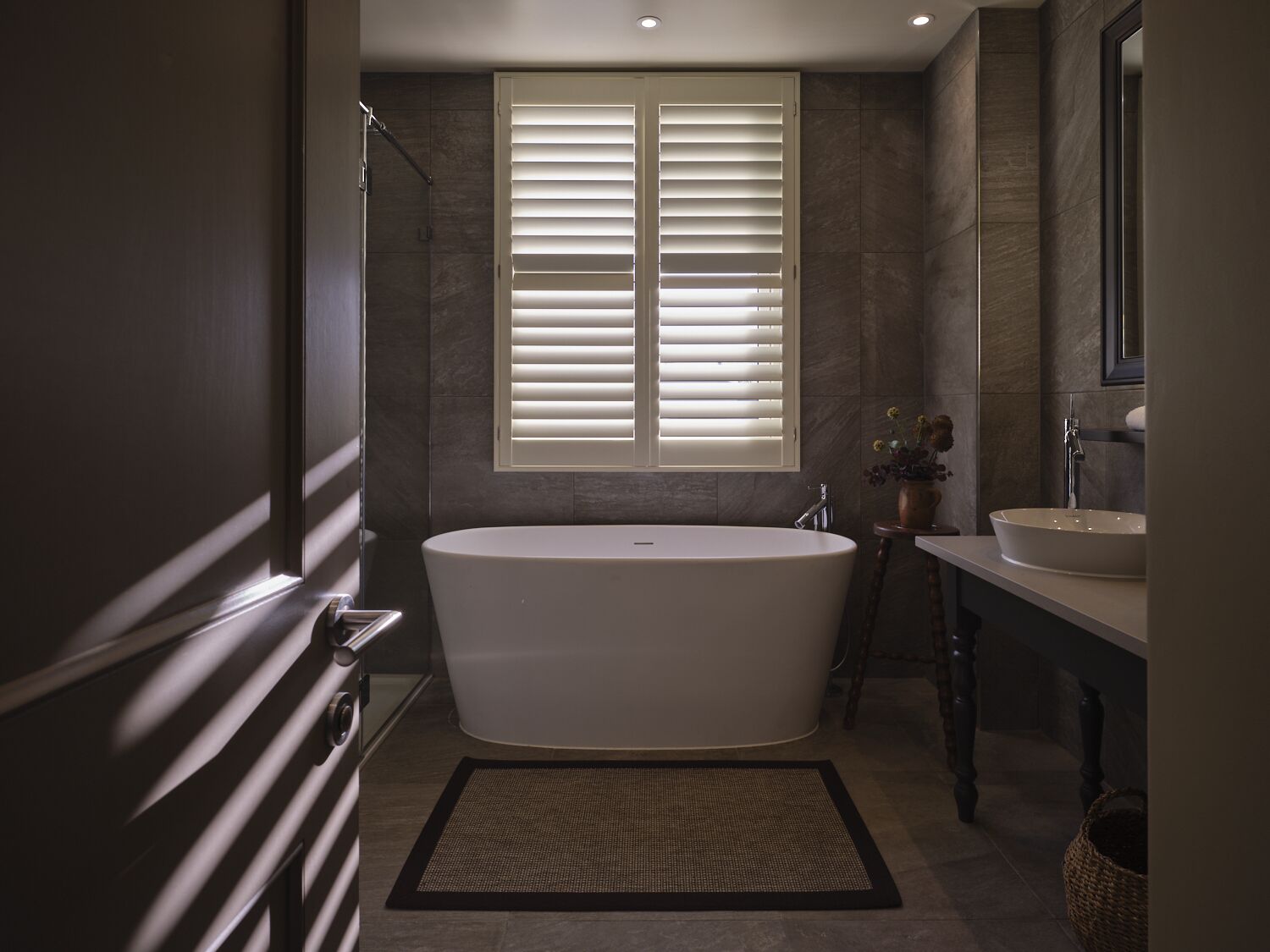 A modern bathroom with a freestanding bathtub, a vanity with a sink, and a window with blinds.