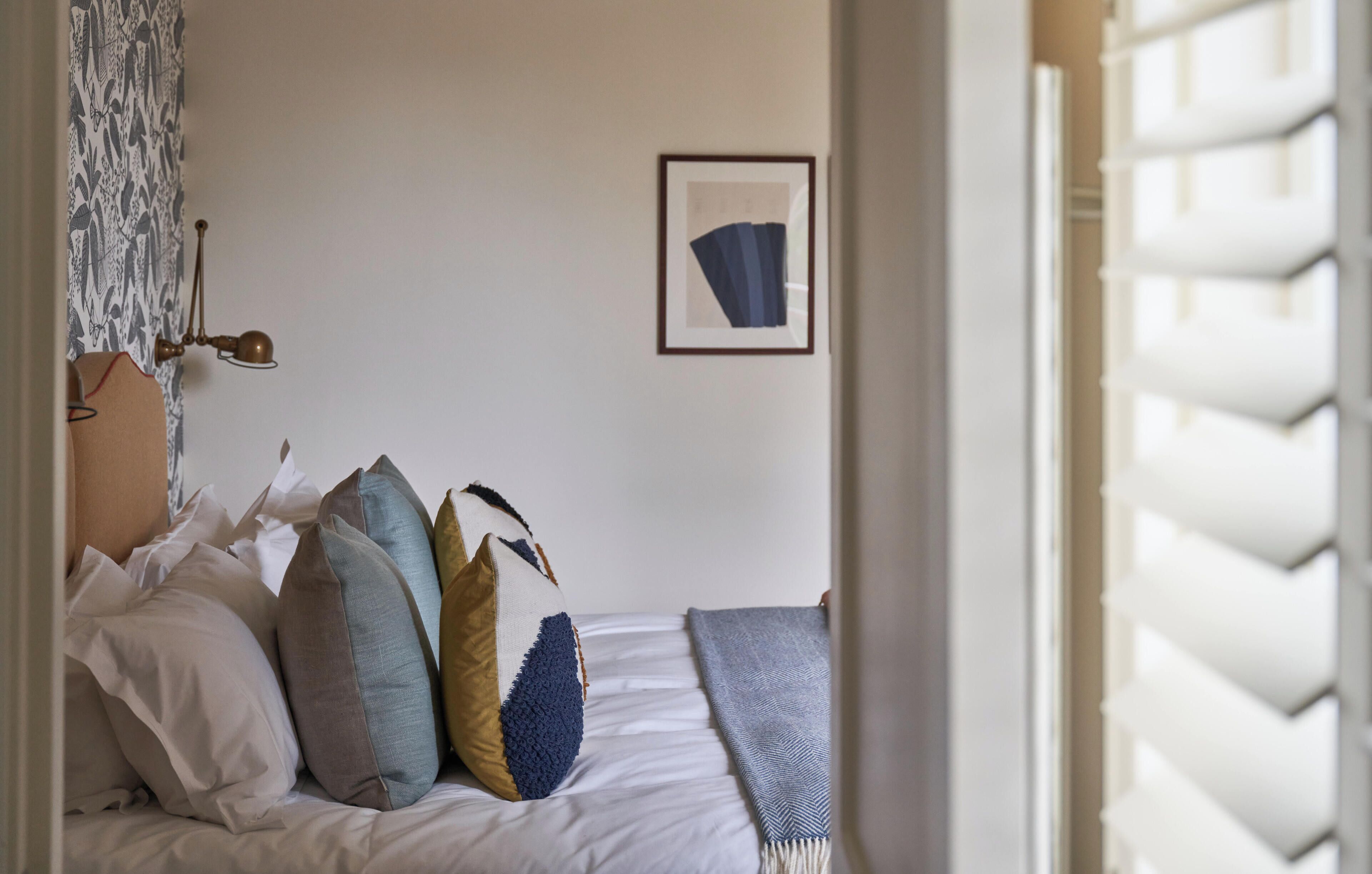 A bedroom with a bed, pillows, a blanket, a wall-mounted picture, and a window with shutters.