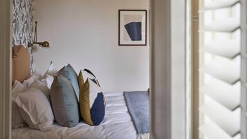 A bedroom with a bed, pillows, a blanket, a wall-mounted picture, and a window with shutters.
