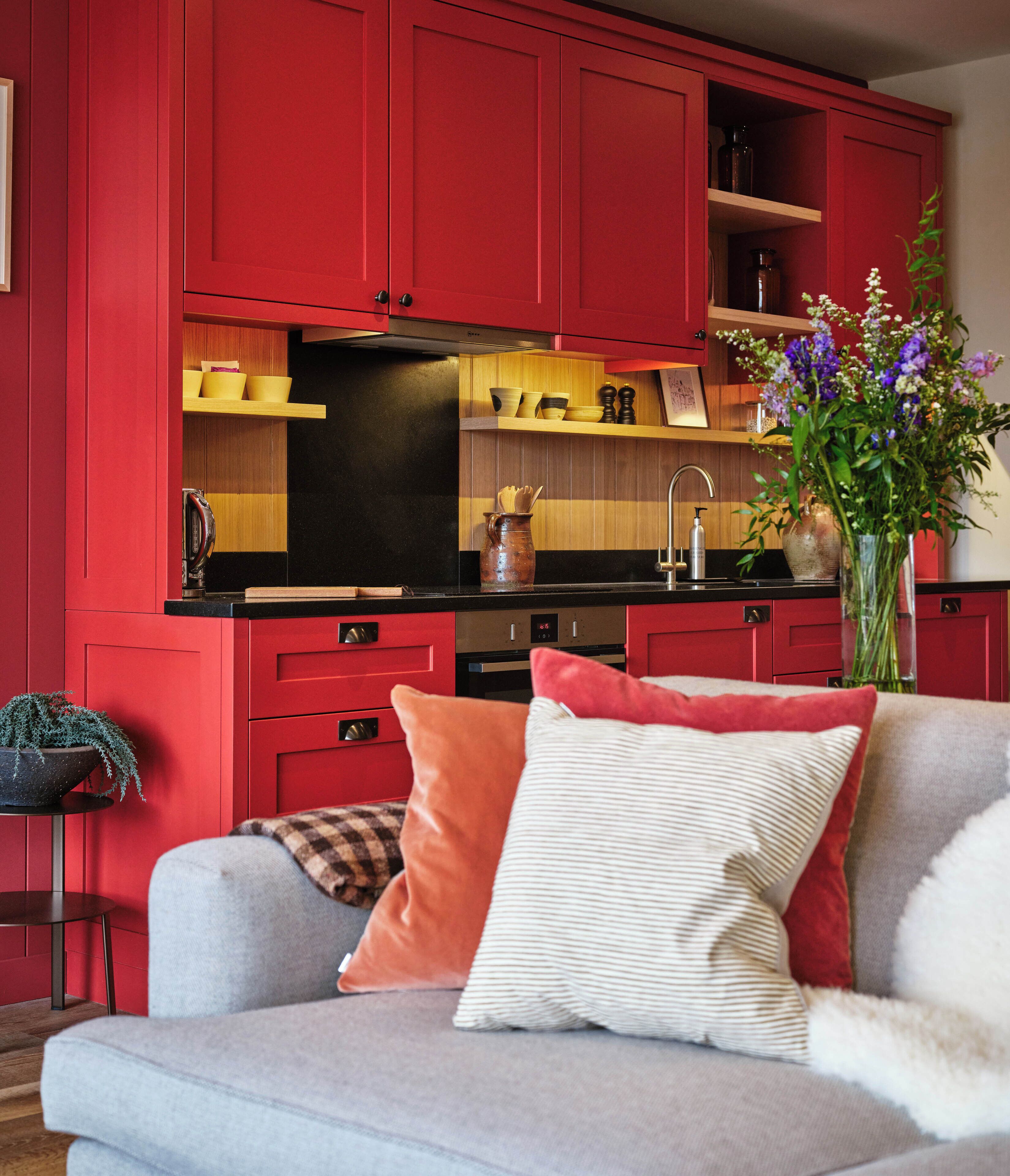 Una cocina moderna con armarios rojos, encimera negra y sofá gris con cojines decorativos.