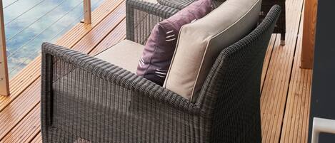 A deck with wicker furniture, a table with cushions, and a view of a lake.