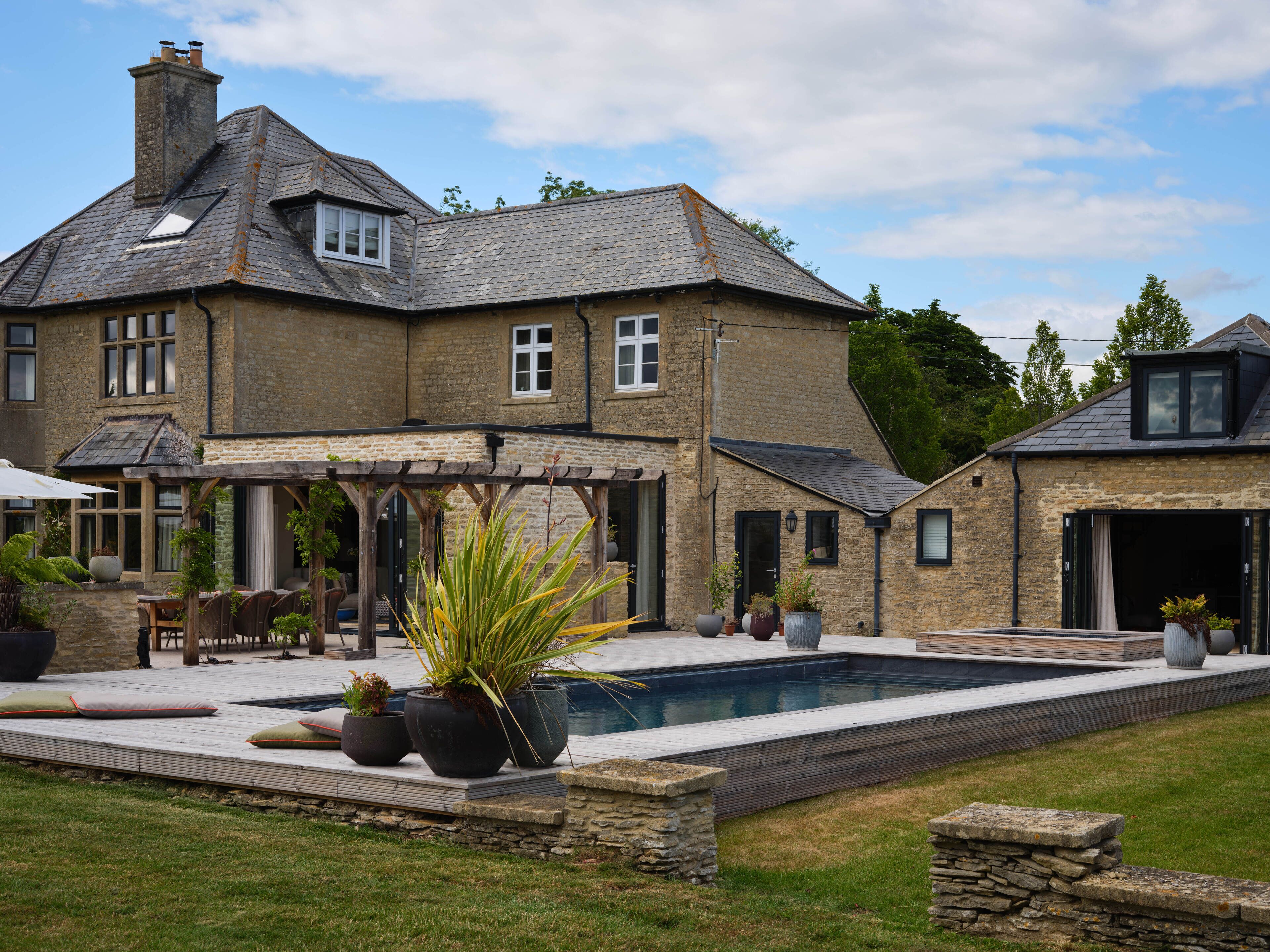 A stone house with a swimming pool, outdoor seating, and potted plants.