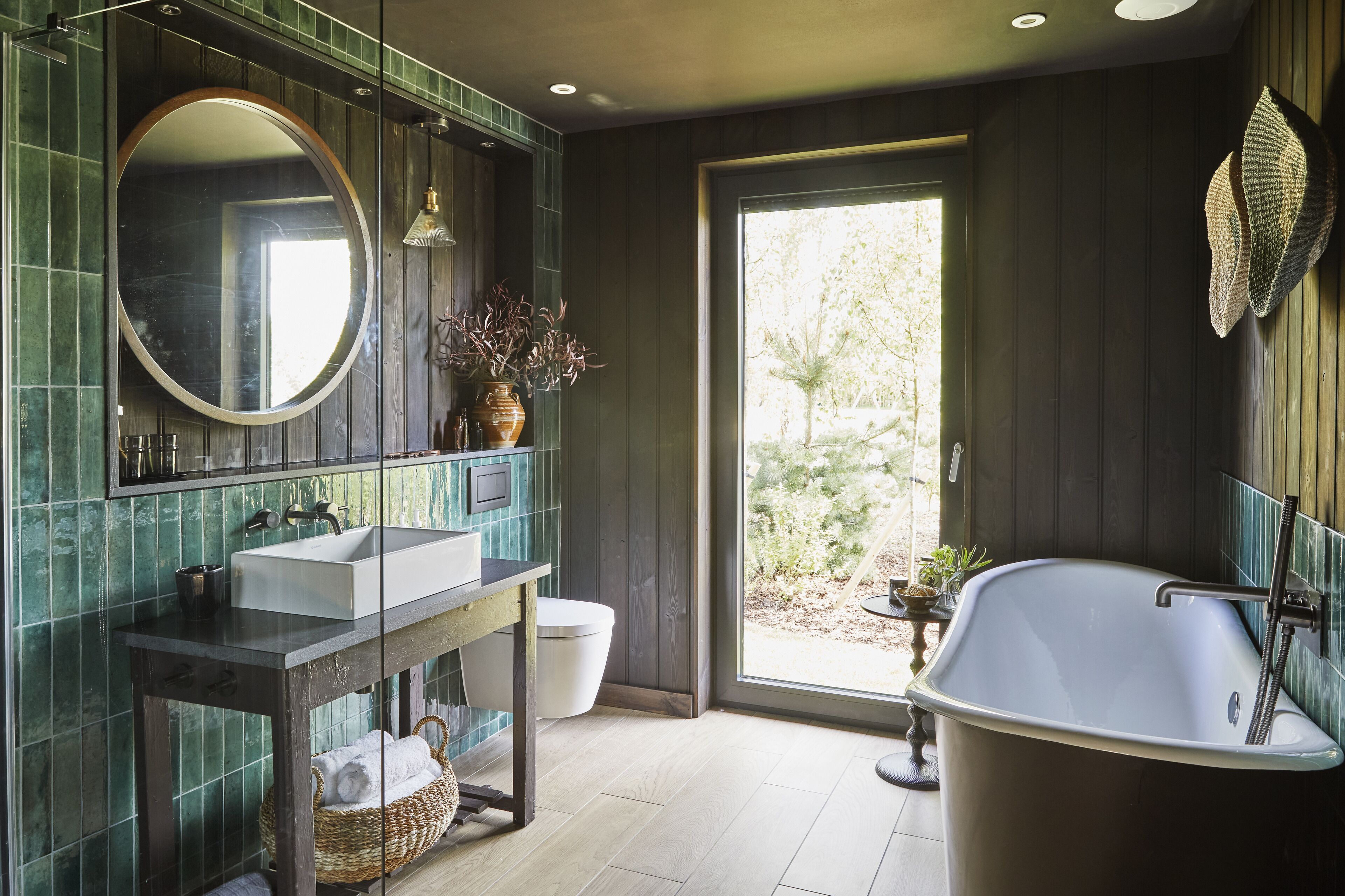 A bathroom with a large mirror, a sink, a bathtub, and a window providing a view of greenery outside.