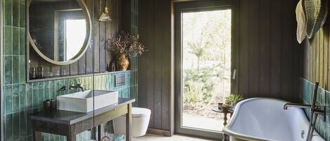 A bathroom with a large mirror, a sink, a bathtub, and a window providing a view of greenery outside.