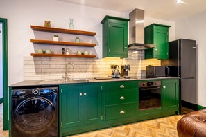 Een keuken met groene kastjes, een wasmachine, een magnetron en een koelkast.