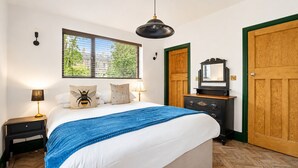 Un dormitorio con una cama, lámparas de noche, un aparador, un espejo y una ventana con persianas.