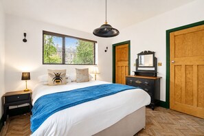 Een slaapkamer met een bed, nachtlampjes, een dressoir, een spiegel en een raam met zonwering.