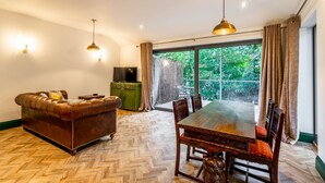 Un área de comedor con piso de madera en patrón de espiga, un sofá de cuero, una mesa de comedor con sillas y un televisor sobre un mueble verde.