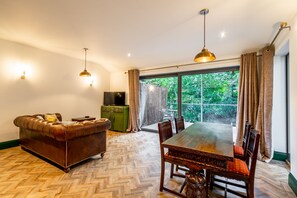 Een zithoek met een houten visgraatvloer, een leren bank, een eettafel met stoelen en een televisie op een groene kast.
