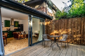 A wooden deck with a sliding glass door leading to a kitchen and living area.