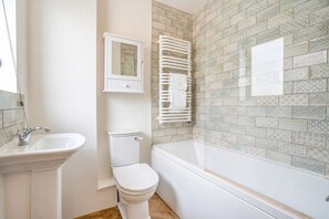 Een badkamer met een wit wastafel, toilet en badkuip. Boven de badkuip bevindt zich een handdoekhouder en boven de wastafel een kastje.