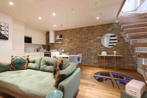 A modern living room with a green sofa, a kitchen area, a brick wall, and a circular mirror. - Unbeatable location! Luxury 2Bed/2Bath Apartment! (London)