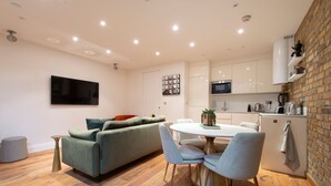 Eine moderne Küche mit weißen Schränken, einem Esstisch mit Stühlen, einem grünen Sofa und einem flachbildfernseher an der Wand.