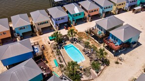 An aerial view of a resort with multiple buildings, a central swimming pool, and a sandy beach area. - Unit 043 - Fish Camp 015 - Pool - Community Boat Ramp - Cute as can be! (Dauphin Island)