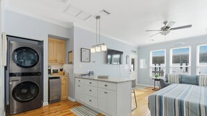 A compact kitchen with a washer and dryer, a small island with a sink, and a large bed with striped bedding. - Unit 043 - Fish Camp 015 - Pool - Community Boat Ramp - Cute as can be! (Dauphin Island)