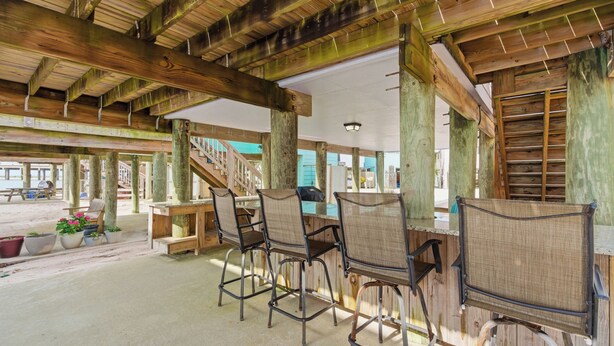 A covered outdoor seating area with wooden beams, metal chairs, and potted plants. - Unit 043 - Fish Camp 015 - Pool - Community Boat Ramp - Cute as can be! (Dauphin Island)