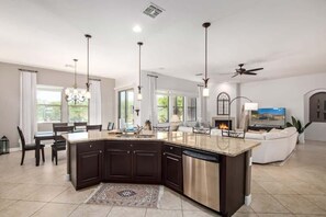 A modern kitchen with dark cabinetry, a stainless steel dishwasher, and a central island. - Luxurious villa with pool and spa (Goodyear)