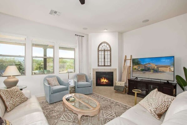A living room with a fireplace, a television, and two armchairs. - Luxurious villa with pool and spa (Goodyear)