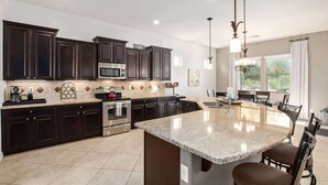 A modern kitchen with dark cabinetry, a central island, stainless steel appliances, and pendant lighting.