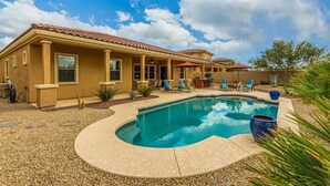 A house with a swimming pool, a patio with chairs, and a small garden.