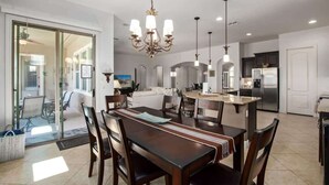 A modern kitchen with a central island, a dining area with a wooden table and chairs, and a chandelier.