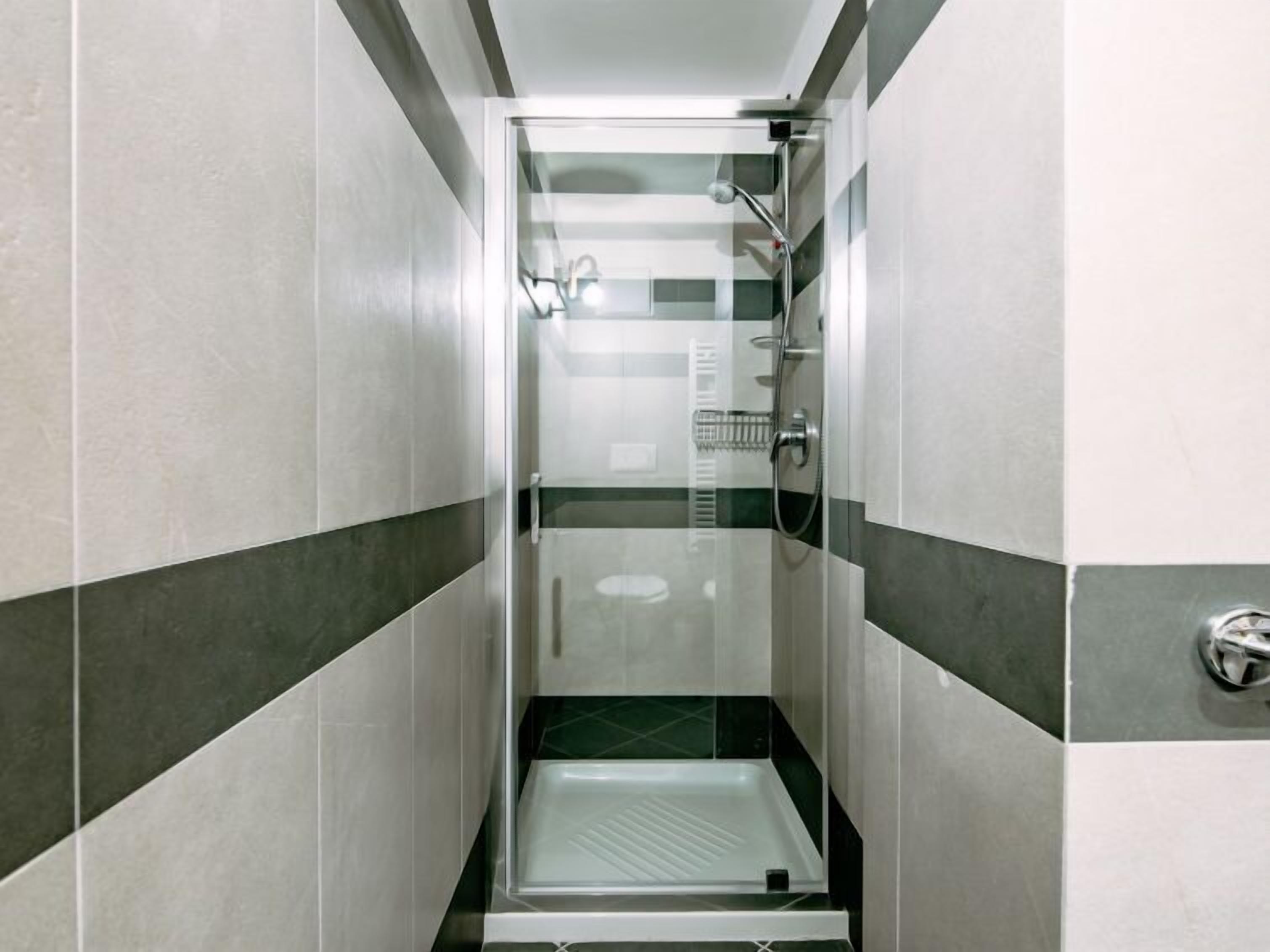 Un petit espace de douche avec une porte en verre, une pomme de douche à main et un robinet fixé au mur.