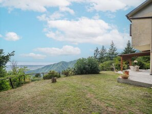 Ein Garten mit Rasen, einer Holzhütte und Blick auf Berge unter blauem Himmel.