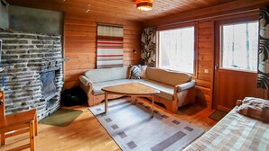 Ein gemütliches Blockhaus-Interieur mit Kamin aus Stein, Holzwänden, einer Couch und einem Fenster mit Vorhängen.