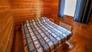 Ein Zimmer in einer Holzhütte mit einem Bett, einem Fenster mit Vorhängen und einer Heizung.