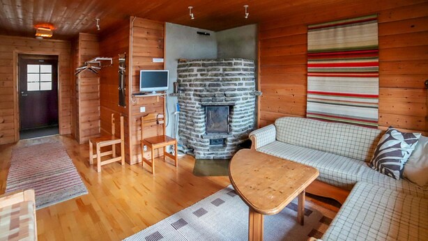 Ein gemütliches Blockhaus-Interieur mit Kamin, Holzwänden, einer Couch und einem Fernseher.
