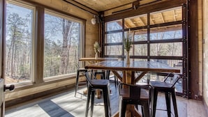 A wooden interior with a large table and chairs, large windows with a view of trees, and a wooden ceiling. - HIBERNATION STATION - 12 Bedrooms with a pool! (Sevierville)