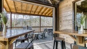 A wooden deck with outdoor seating, including tables and chairs, and a covered area with a glass roof. - HIBERNATION STATION - 12 Bedrooms with a pool! (Sevierville)