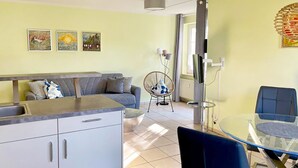 Une cuisine moderne avec un plan de travail gris, des armoires blanches et une chaise bleue. On y trouve également un coin repas avec une table et des chaises en verre.