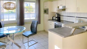 Une cuisine moderne avec un coin repas, comprenant une table en verre, des chaises et une vue sur l’extérieur.