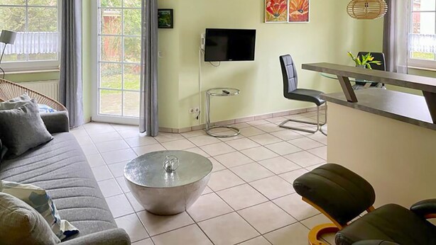 Un salon comprenant un canapé, une table basse, un téléviseur, un coin repas avec une chaise, et une fenêtre avec des rideaux.