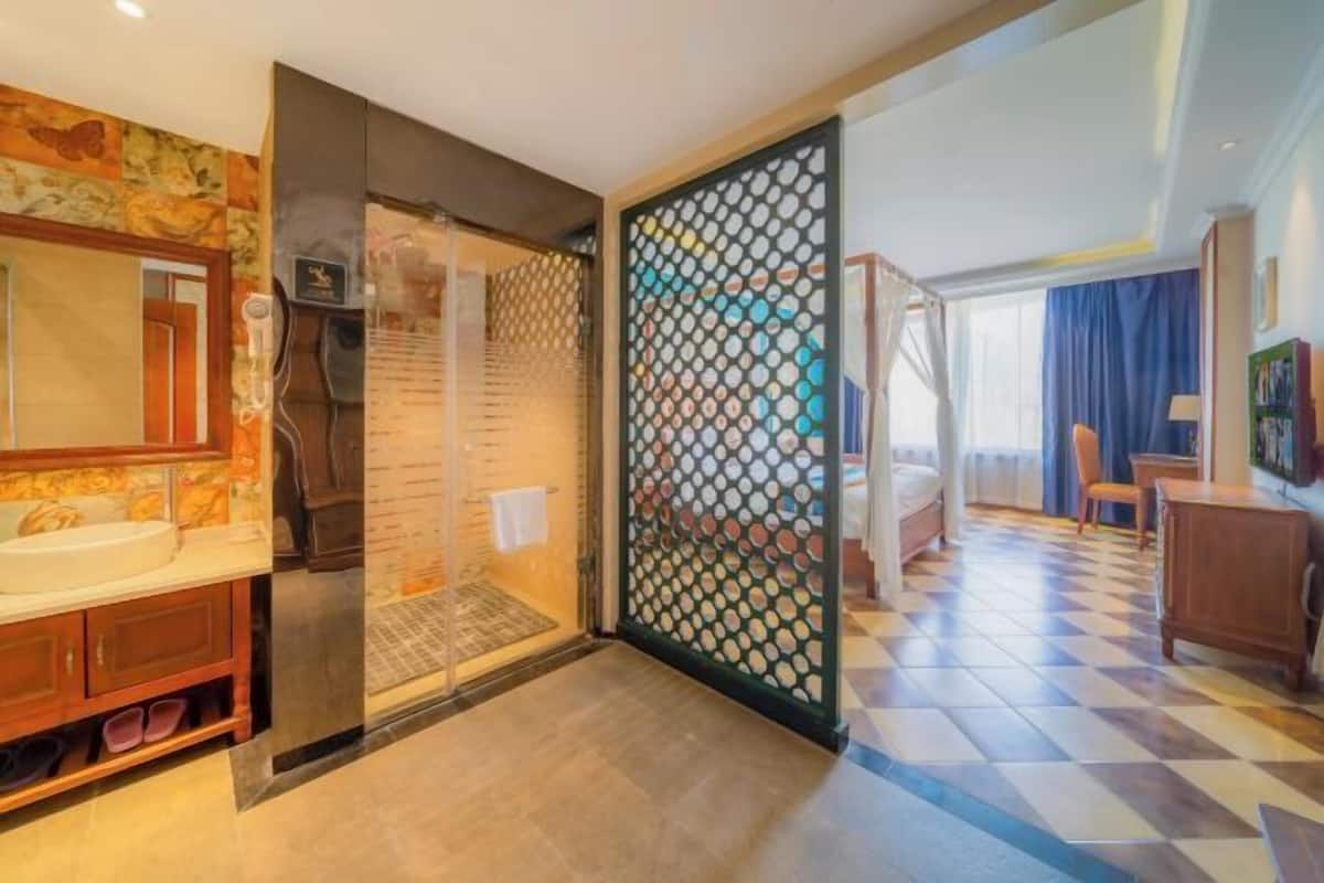 A hotel room with a bathroom featuring a large mirror, a sink, and a shower. There is a sliding door leading to the bedroom.