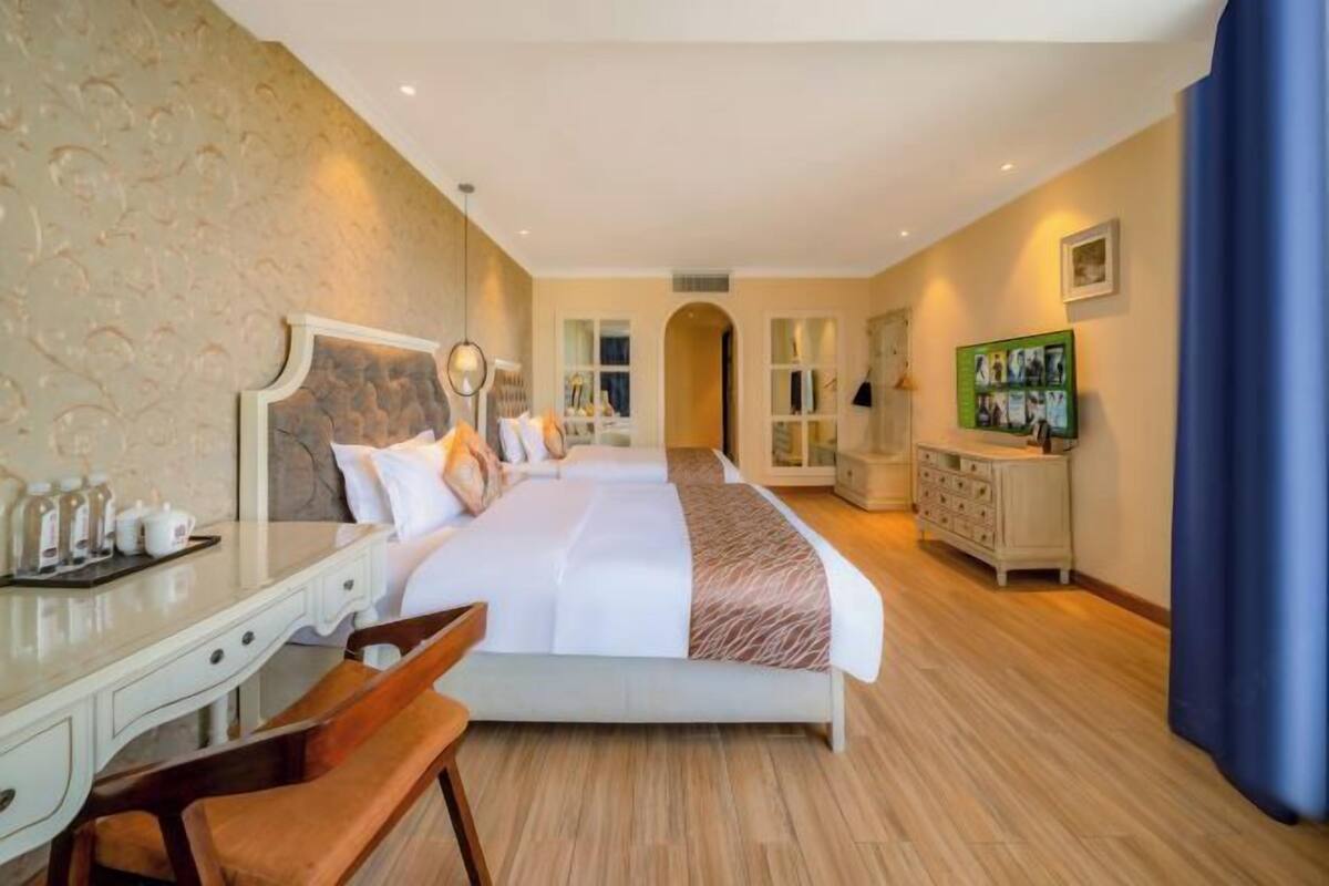 A hotel room with a large bed, a desk, a chair, a dresser, and a television.