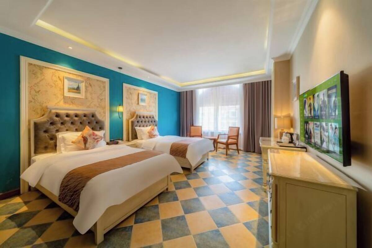A hotel room with two beds, a desk, and a TV.