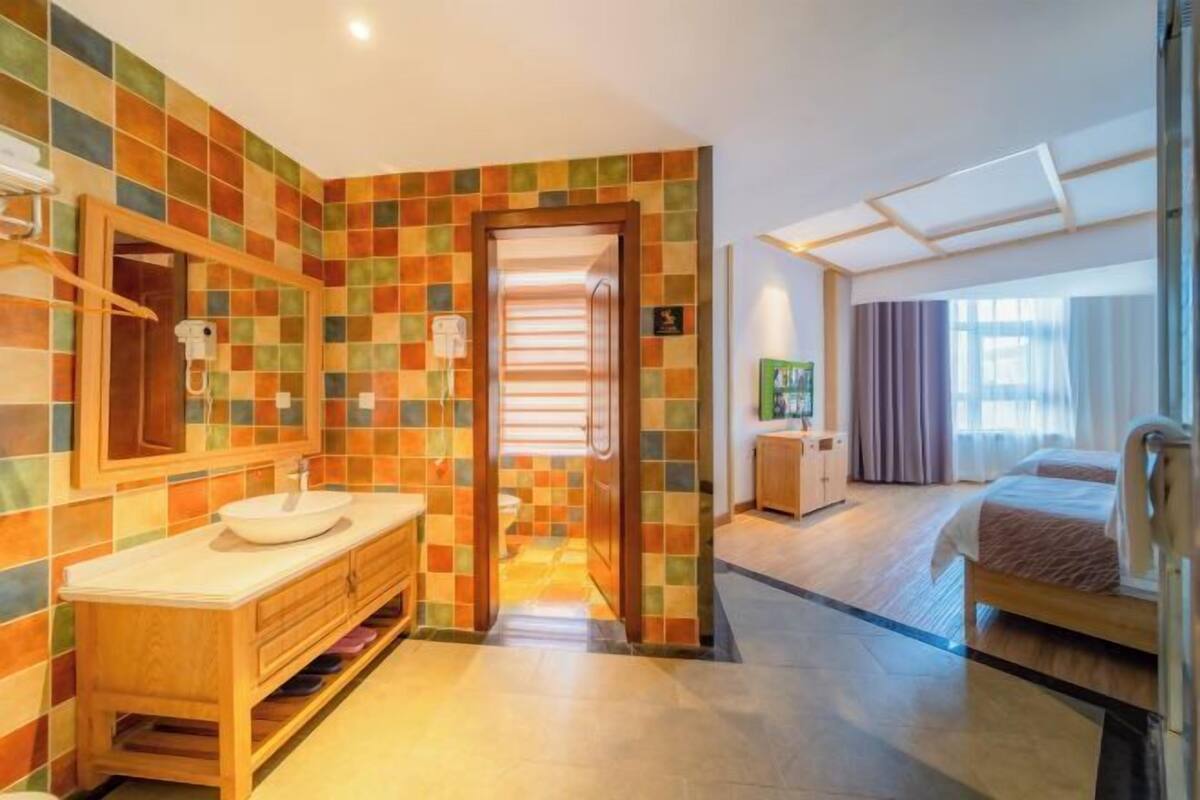 A hotel bathroom with a tiled wall, a wooden vanity, a sink, and a mirror.