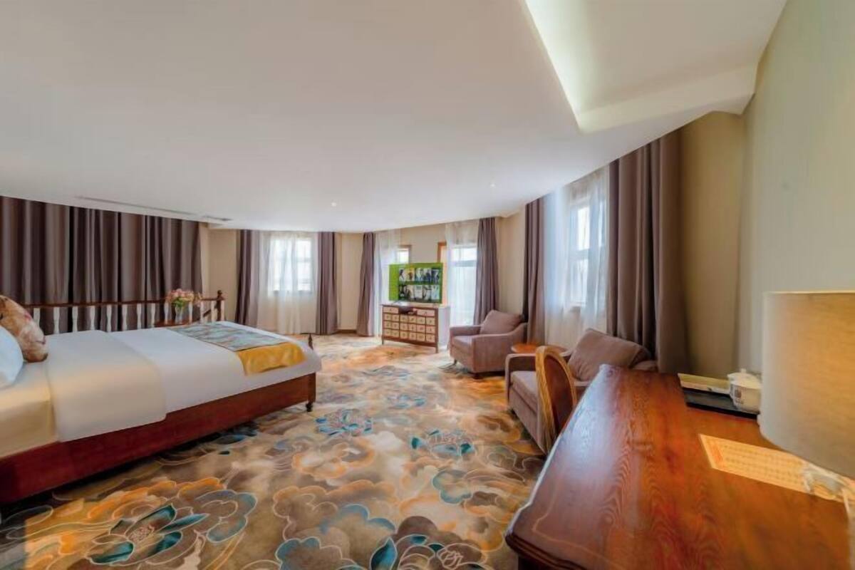 A hotel room with a bed, a sofa, a desk, and a view of a cityscape.
