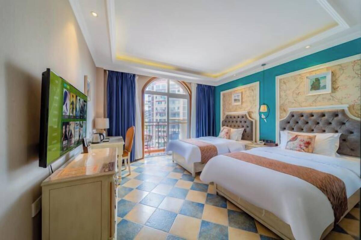 A hotel room with two beds, a desk, a TV, and a large window.