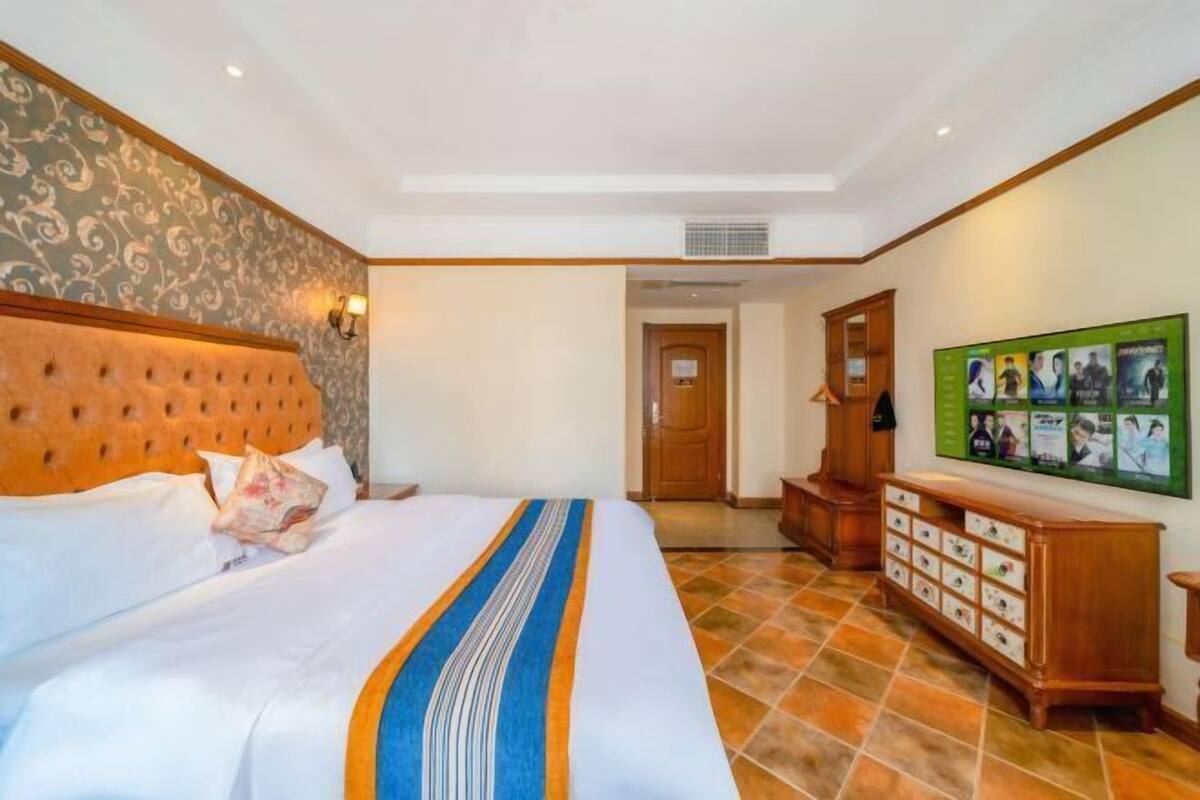 A hotel room with a large bed, a headboard, a wall-mounted TV, and a wooden cabinet.