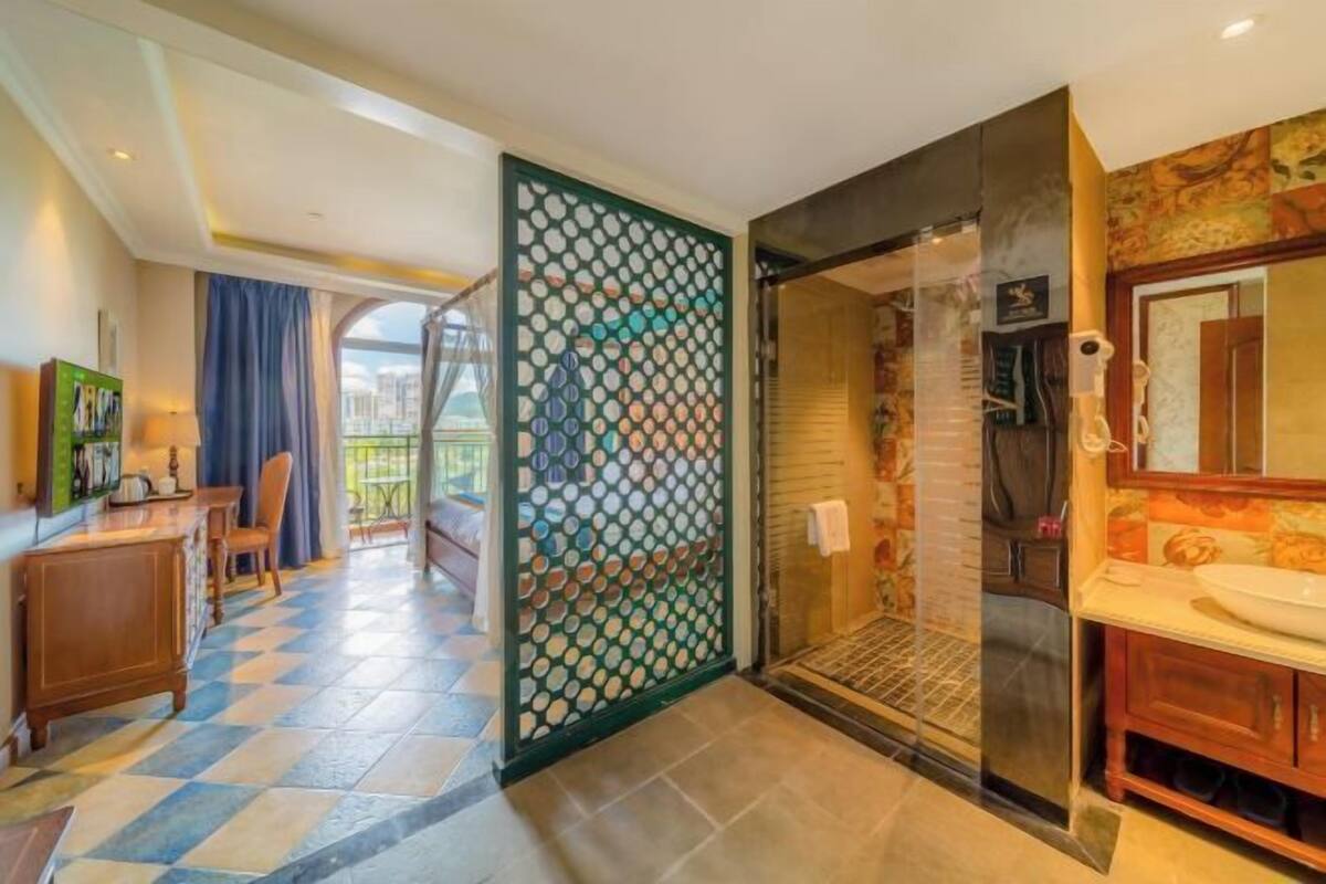A hotel room with a checkered floor, a bathroom with a large mirror, and a view of the outdoors.