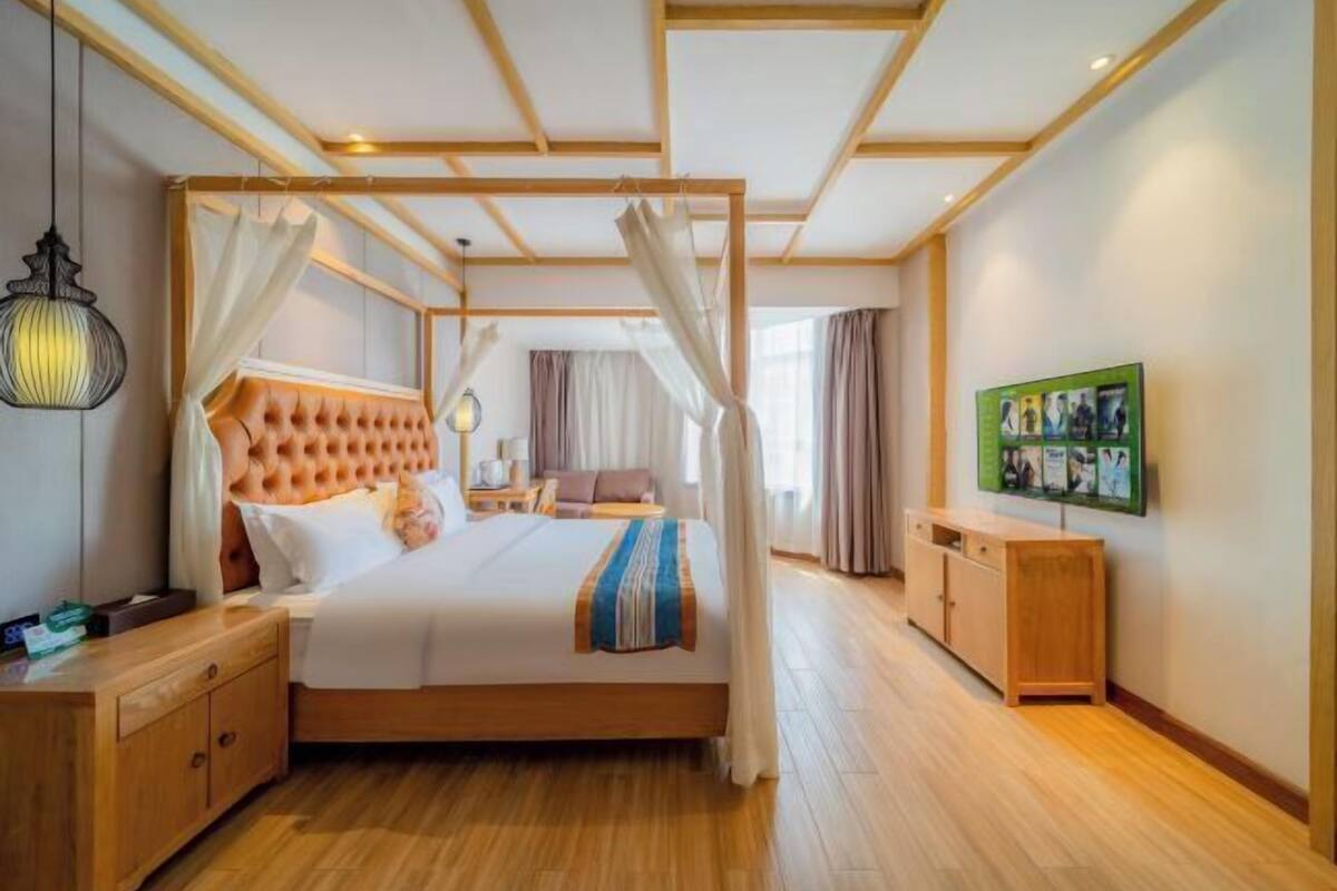 A bedroom with a four-poster bed, wooden headboard, bedside tables, a nightstand, a wardrobe, and a television on the wall.