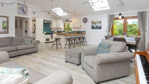 Un salón amplio con un piano, sofás y una zona de cocina con barra.