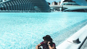 Una persona seduta a bordo piscina, con un'architettura moderna sullo sfondo.