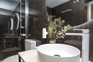 Ein modernes Badezimmer mit einem weißen Waschbecken, einer Duschkabine aus Glas und einer Wand mit Marmorplatten.