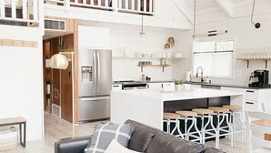 A spacious loft-style apartment with a high ceiling, a kitchen with white cabinetry, a dining area with a wooden table, and a leather sofa with cushions. - White Mtns Cabin | Balcony | Fireplace | Grill (Pinetop)